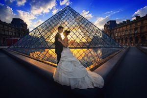 Couple embraces before the Louvre Pyramid during a stunning sunset in Paris.